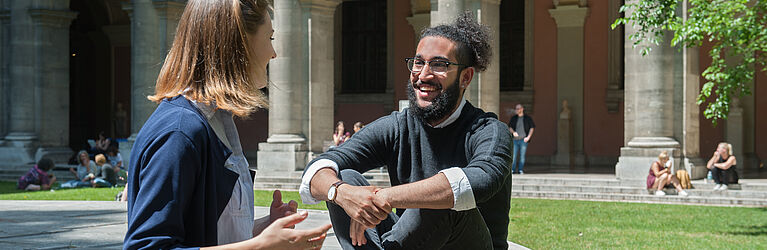 A female and a male student talk to each other while sitting in inner courtyard of the University Eine Studentin und ein Student  unterhalten sich sitzend im Innenhof der Universität