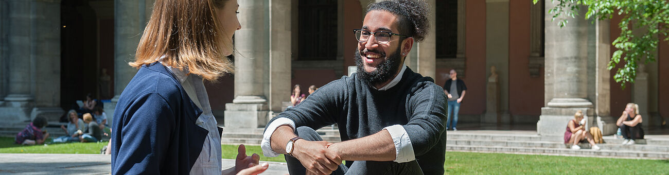 A female and a male student talk to each other while sitting in inner courtyard of the University Eine Studentin und ein Student  unterhalten sich sitzend im Innenhof der Universität